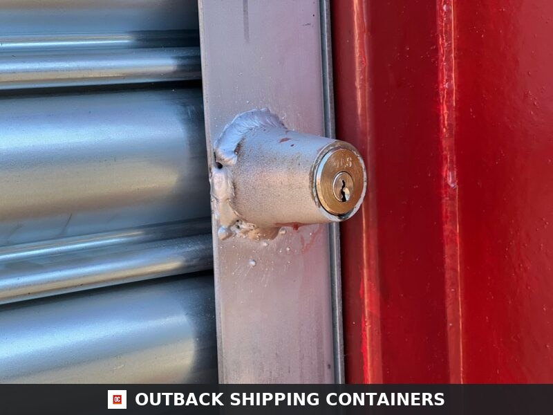 Bullet lock and housing welded to a grey roller shutter door track on a red 20ft used shipping container