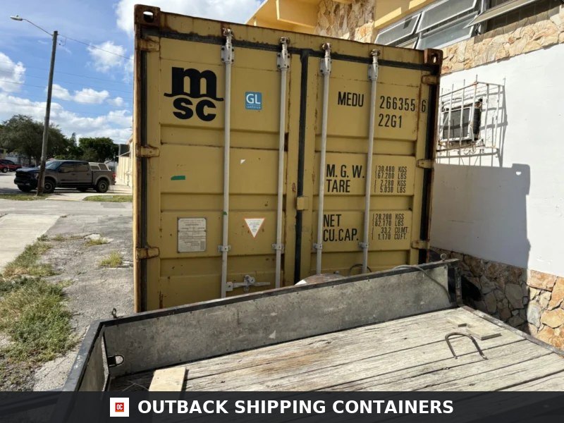 Used 20ft Conex Shipping / Storage Container – Yellow/Gold for Sale — Window and Shutter Detail Rear cargo doors of a used 20ft yellow shipping container showing locking bars and MSC branding next to a building