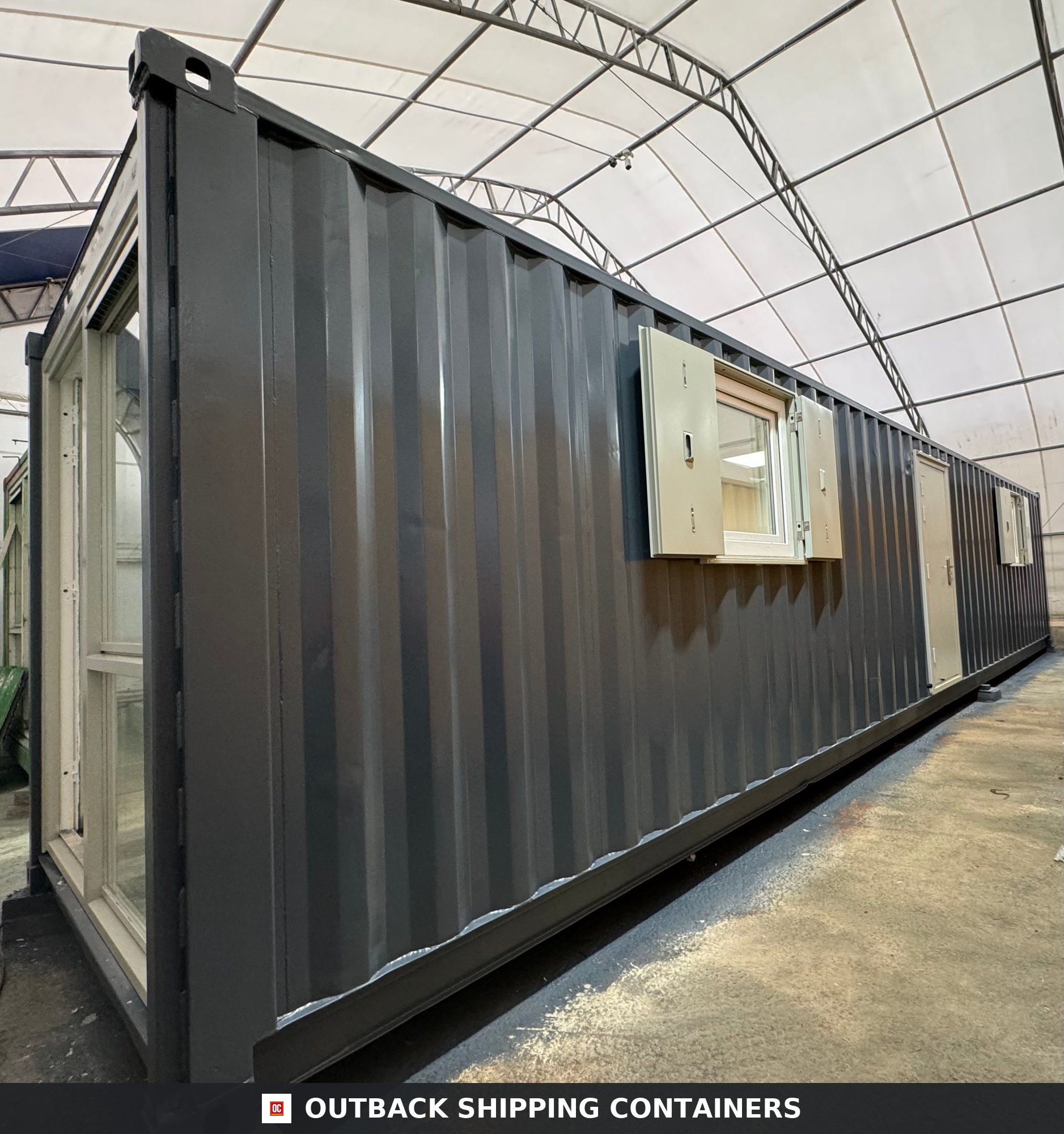 Dark grey 40ft converted shipping container office with open shutters and a side entry door in a warehouse