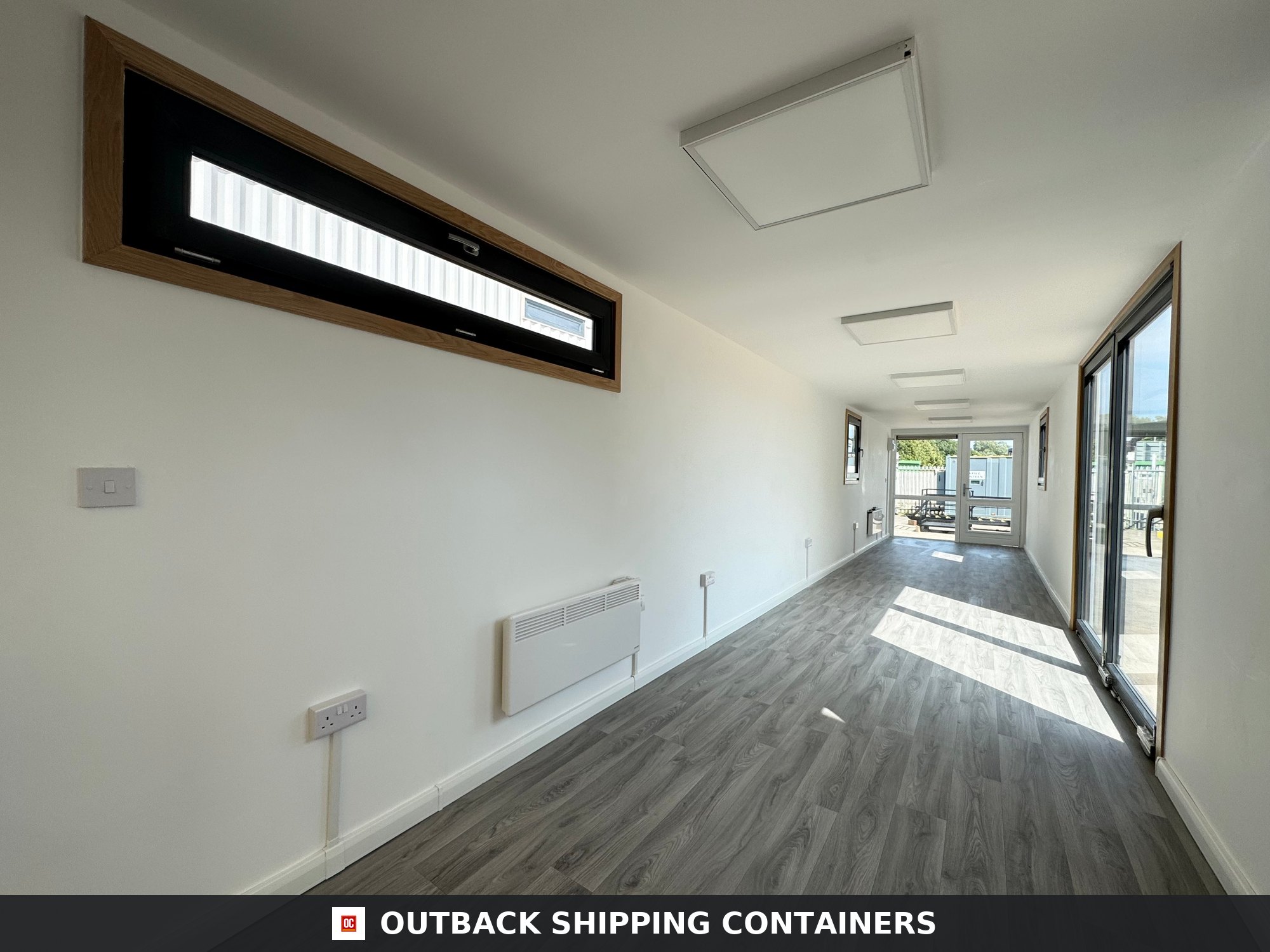 40ft shipping container office interior with wood floors, white walls, horizontal windows, and flat panel lighting