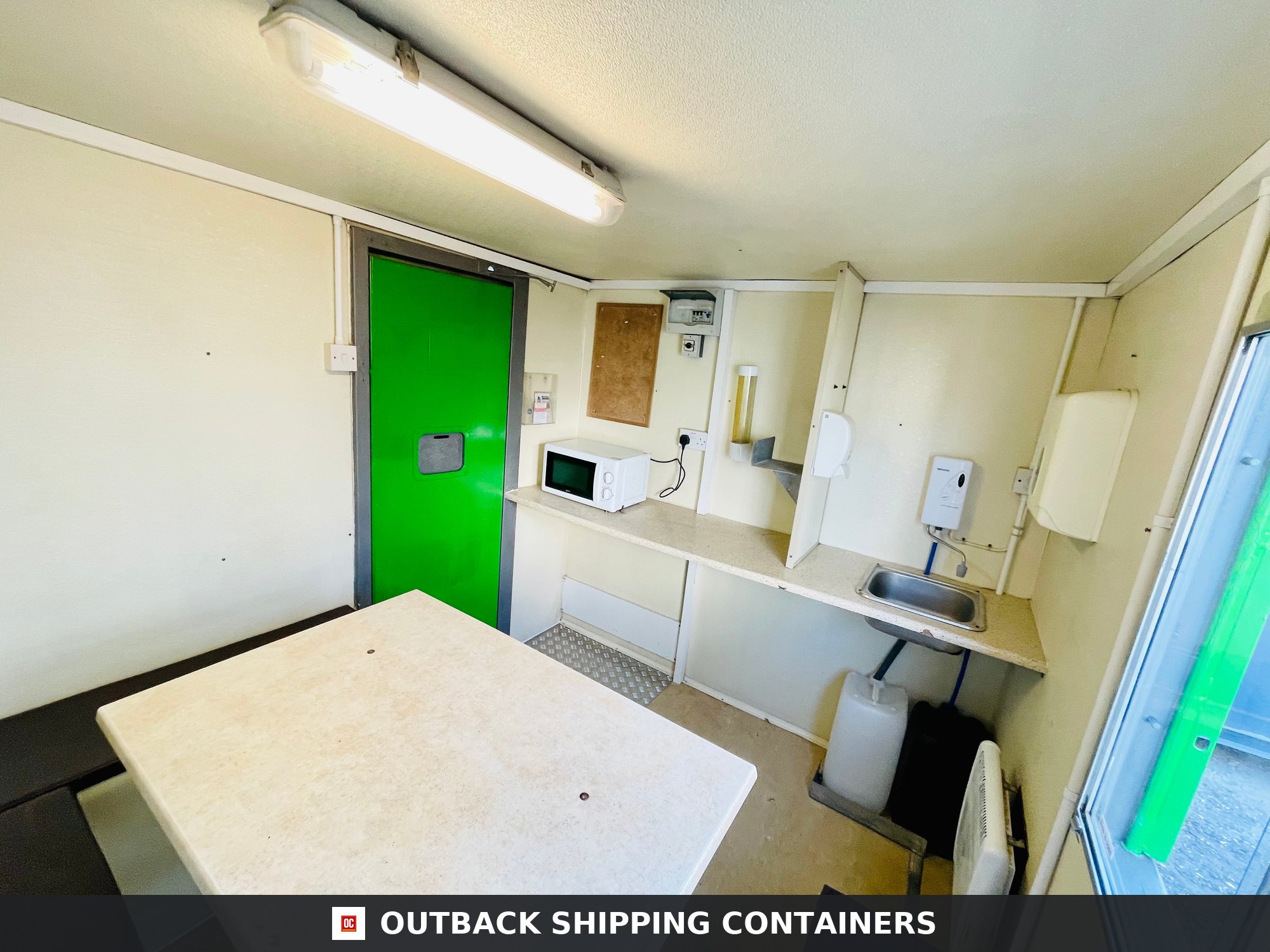 Towable Groundhog Mobile Welfare |Towable Canteen, Office, WC — Three-Quarter Angle View Interior view of a mobile welfare unit featuring a canteen with table, microwave, and sink next to a bright green door