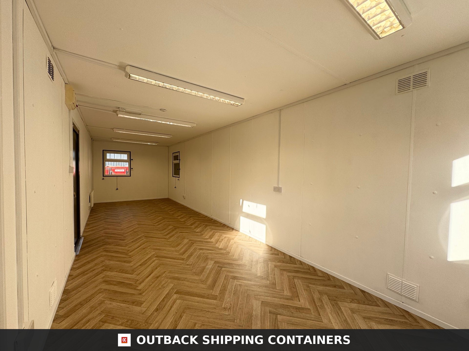 32ft Cabin for Sale — Roof and Structural Detail | Outback Shipping Containers 2 Refurbished 32ft anti-vandal cabin office in dark gray with white framed windows and steel entry door on a dirt lot