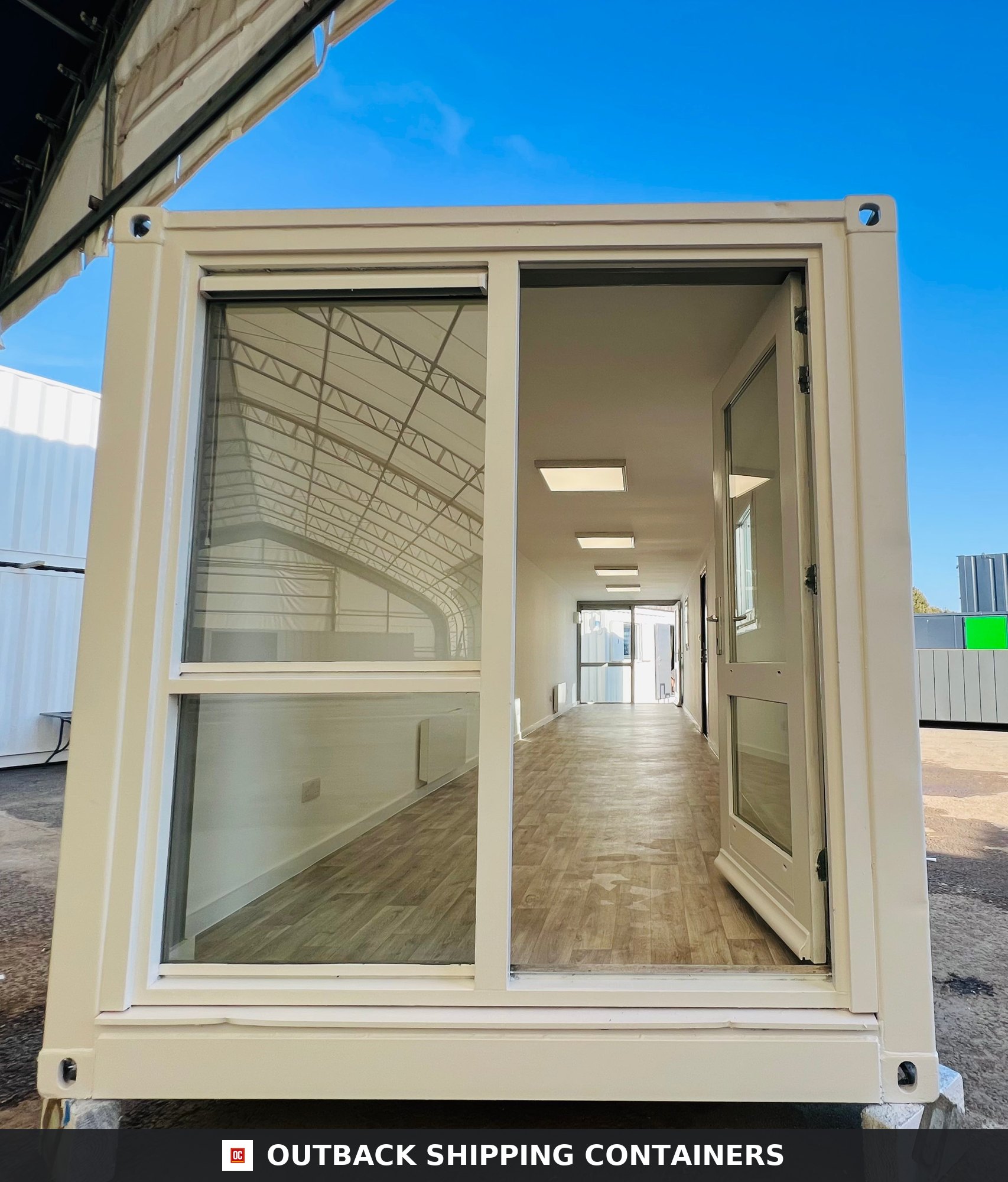 40ft container office exterior view through an open glass door showing a long open plan interior with wood style flooring