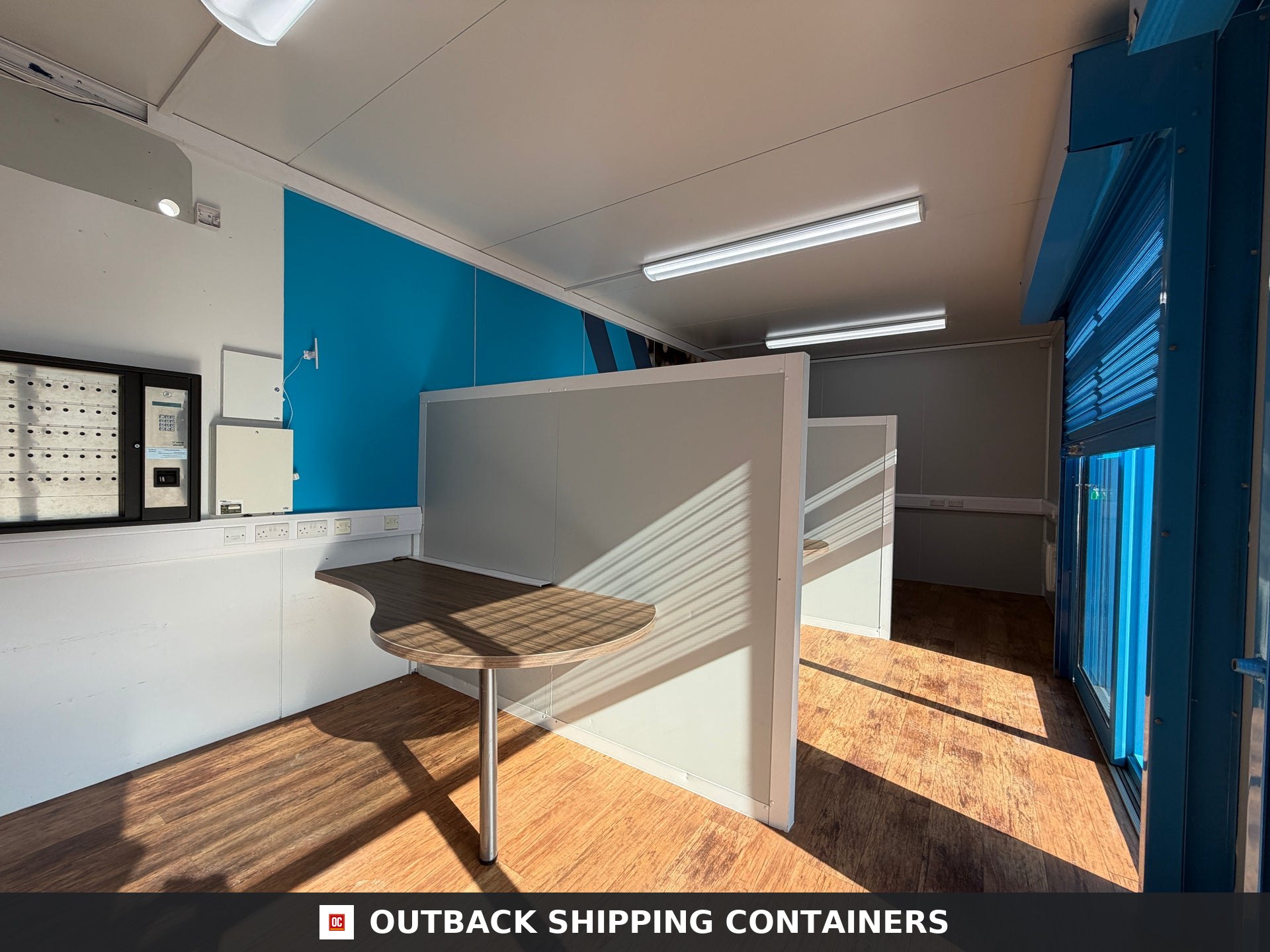 26x12ft for Sale — Door and Entry Detail | Outback Shipping Containers Marketing suite portable building interior showing office desk cubicles with wood floors and blue accent wall