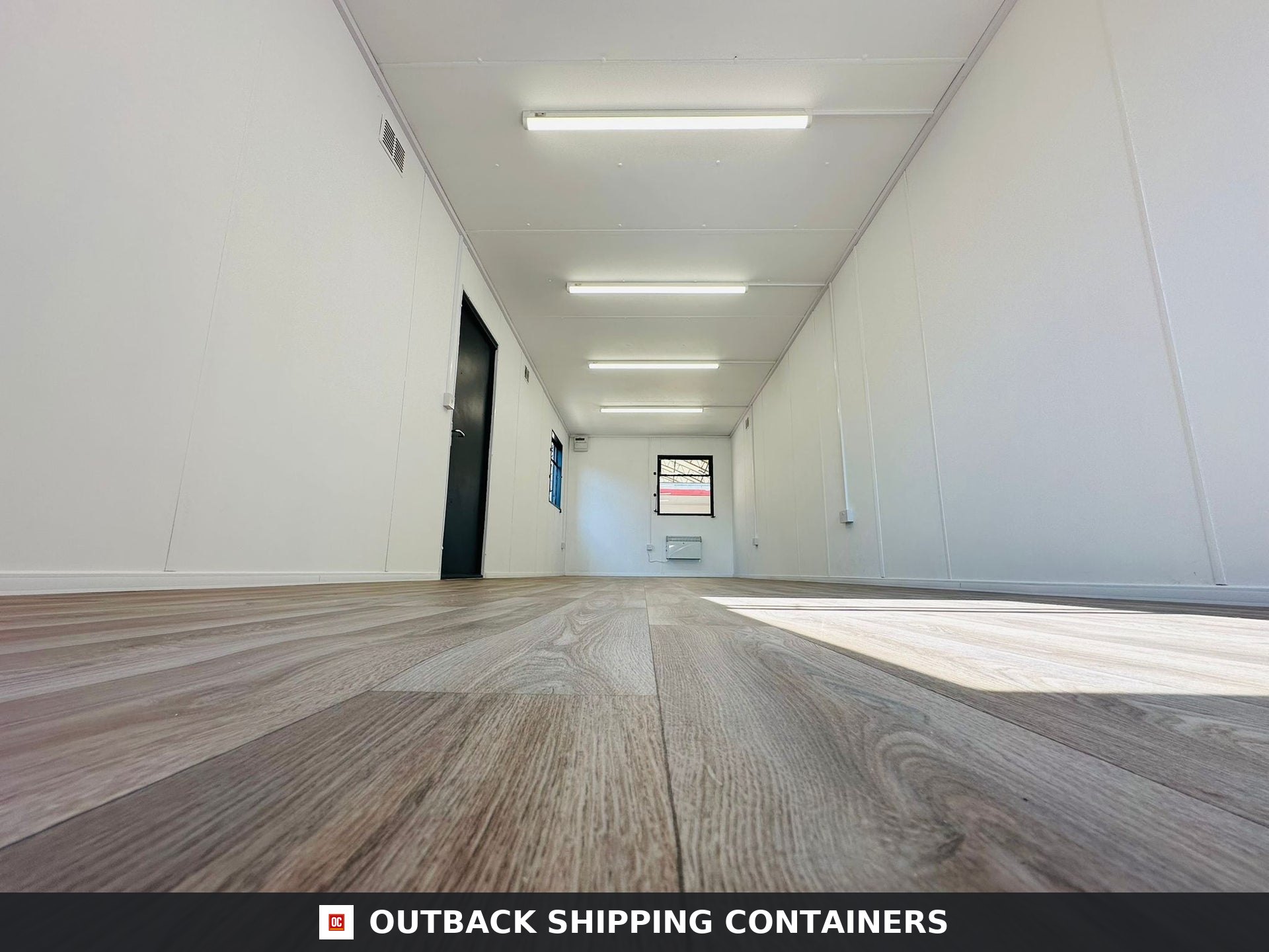 32x10ft Cabin for Sale — Three-Quarter Angle View | Outback Shipping Containers 2 3 Open plan interior of a 32x10 portable office cabin with white walls, wood grain flooring, and overhead LED strip lighting