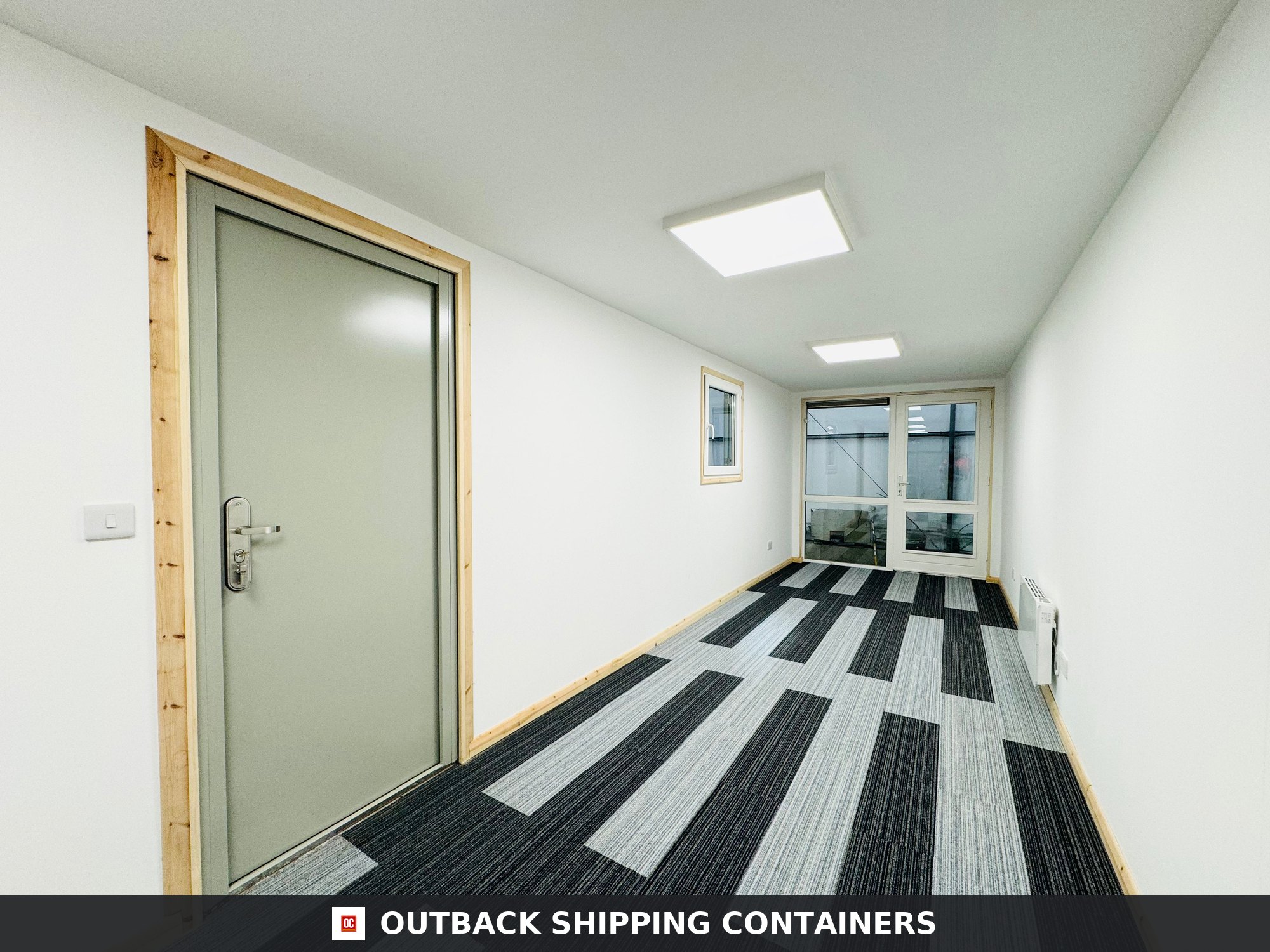 Interior view of a 40ft open plan shipping container office with grey door, striped carpet, and white walls