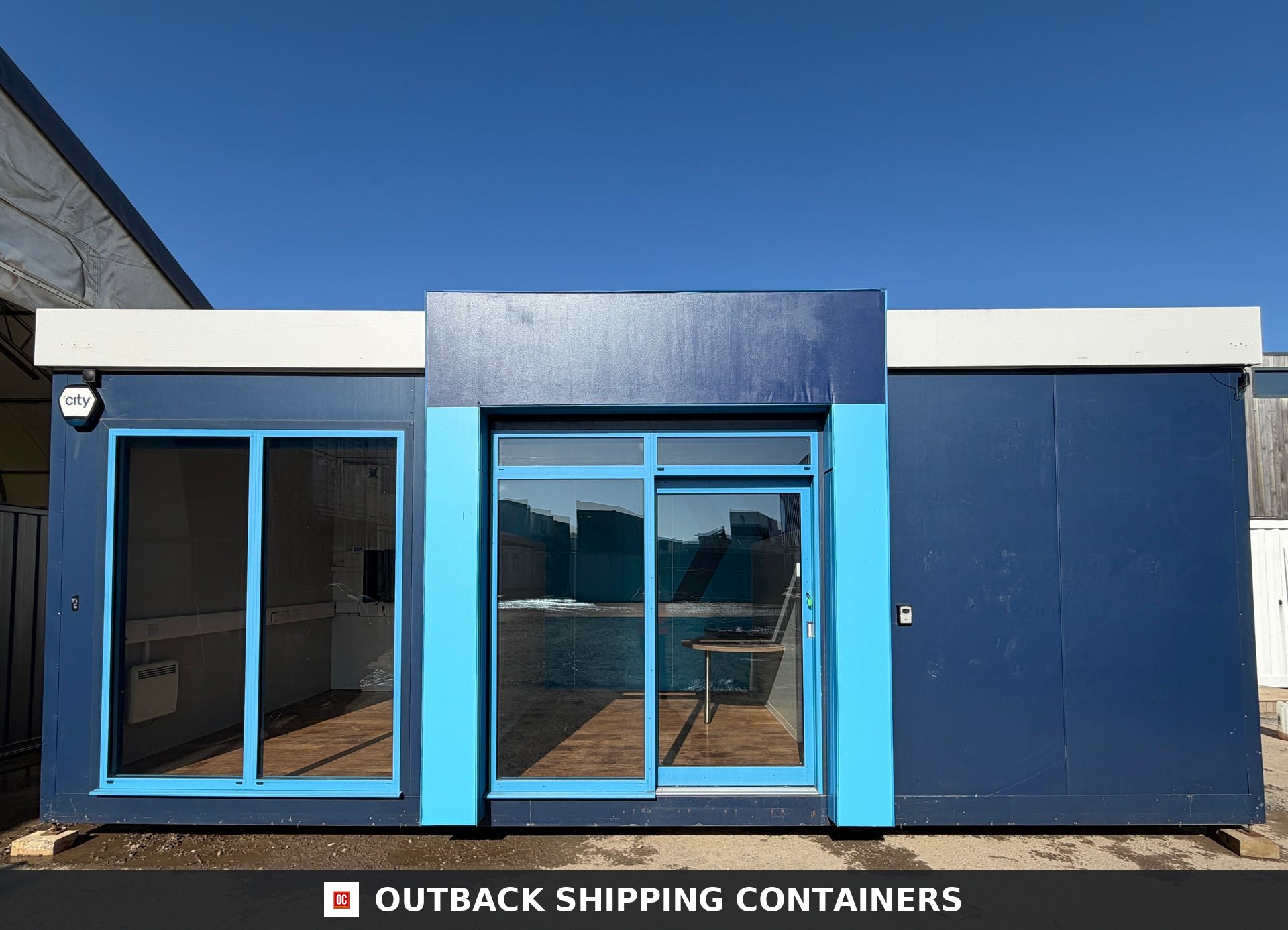 26x12ft for Sale — Interior Detail | Outback Shipping Containers 26x12ft blue marketing suite portable building with glass entry doors and large windows under a clear blue sky