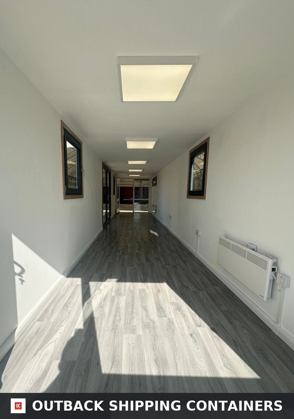 40ft shipping container office interior with white walls, wood floors, flat panel LED lights, and wall heaters