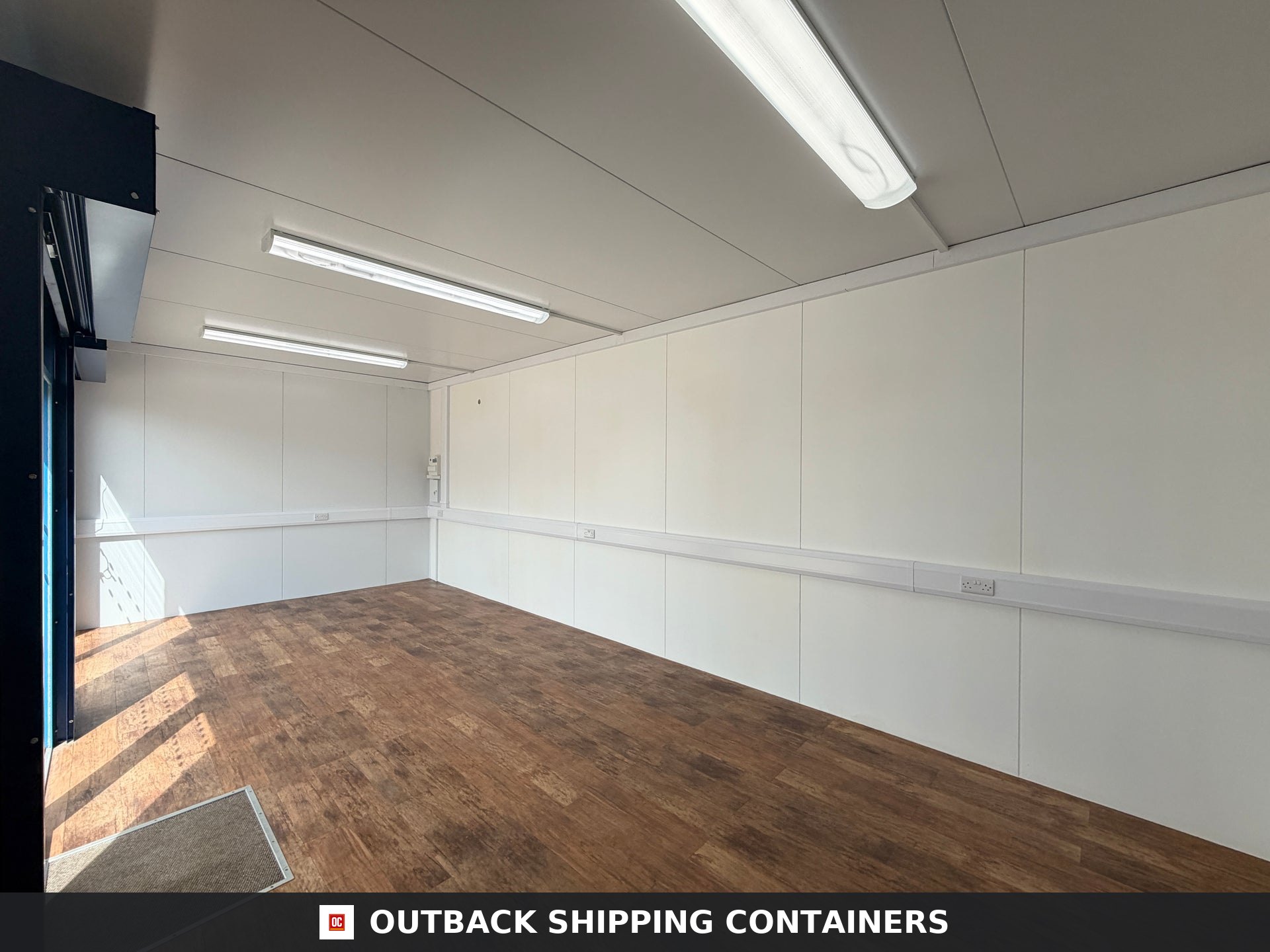 26x12ft for Sale — Side Profile View | Outback Shipping Containers Interior view of a refurbished 26x12 marketing suite featuring wood-style flooring and white walls with LED lighting