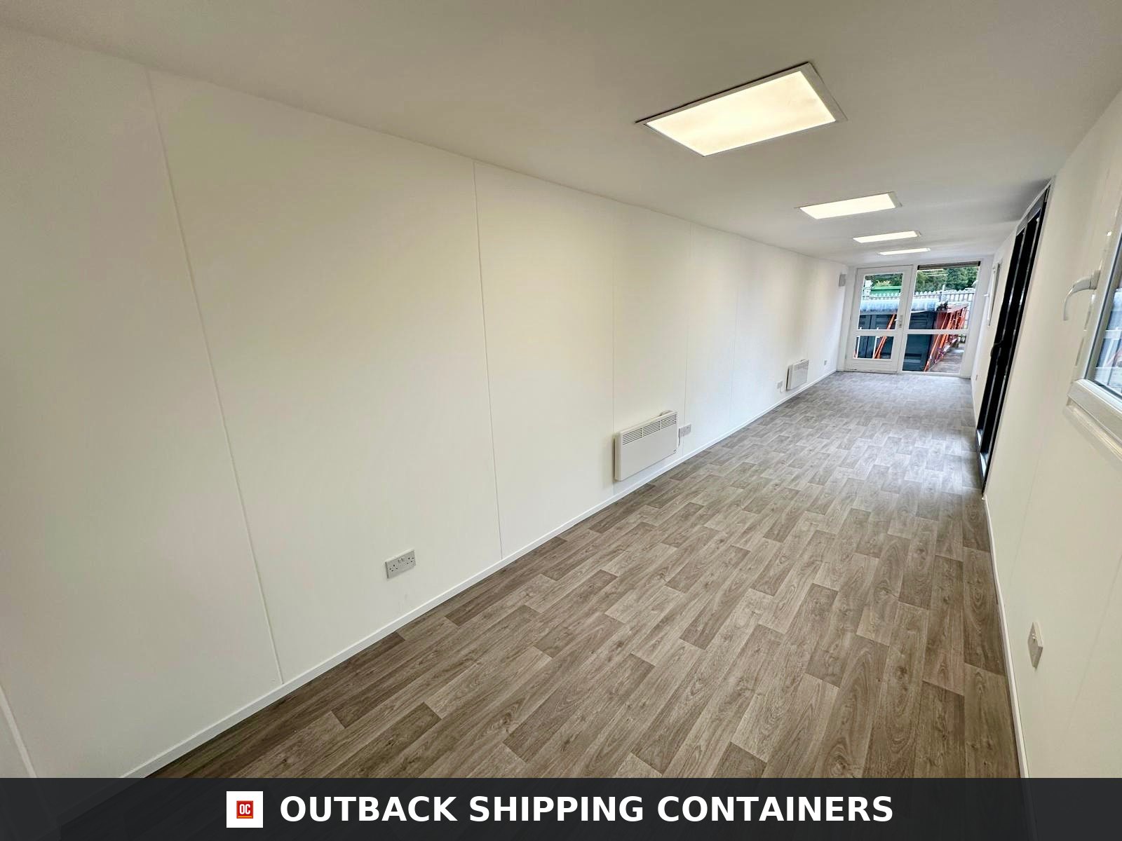 Interior of a 40ft shipping container office with white walls, wood laminate flooring, and recessed ceiling lights