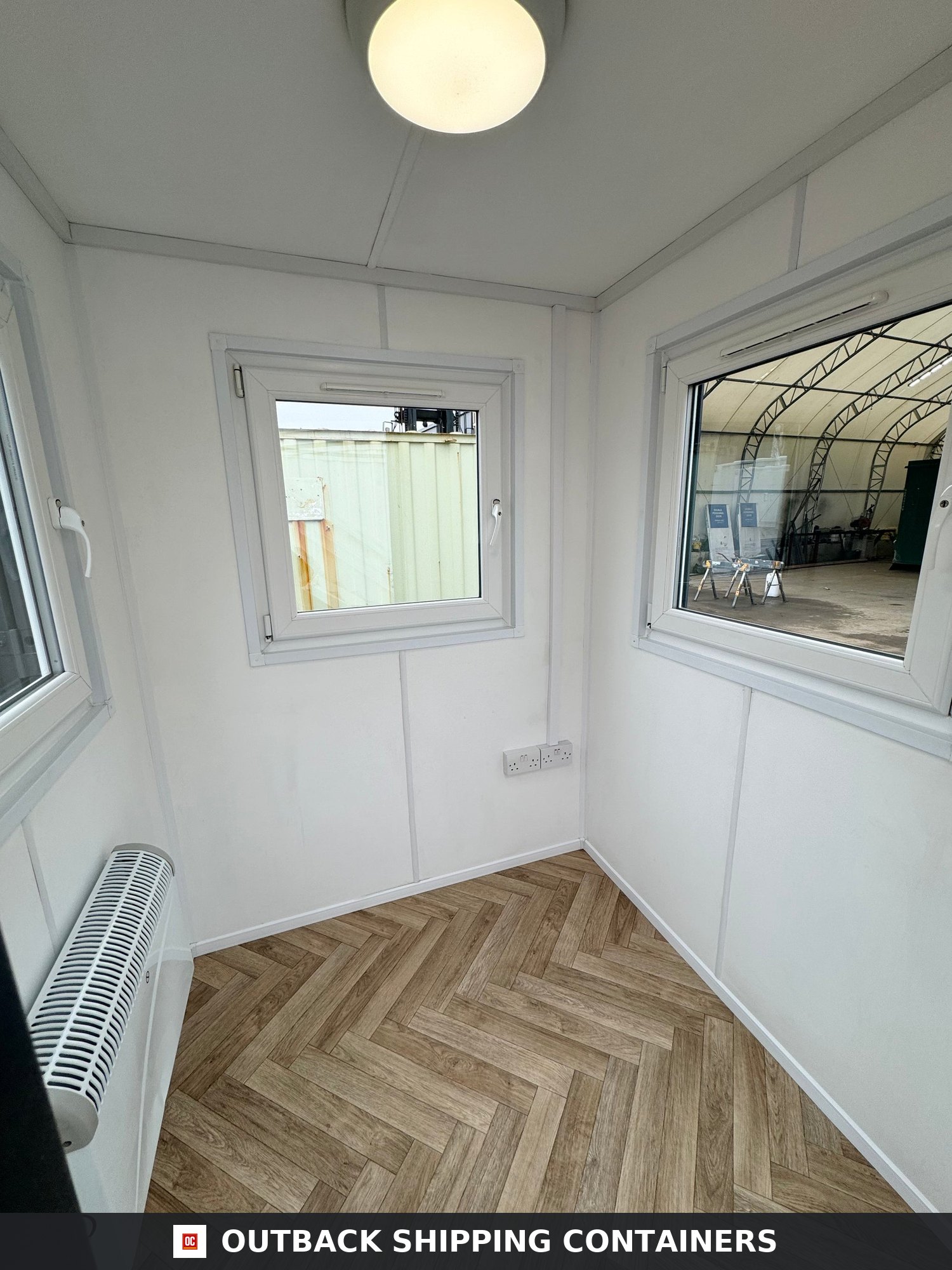 6x6 ft 6x6FT for Sale — Three-Quarter Angle View | Outback Shipping Containers Interior of a refurbished 6x6 gate house office with parquet flooring white walls windows and a convection heater