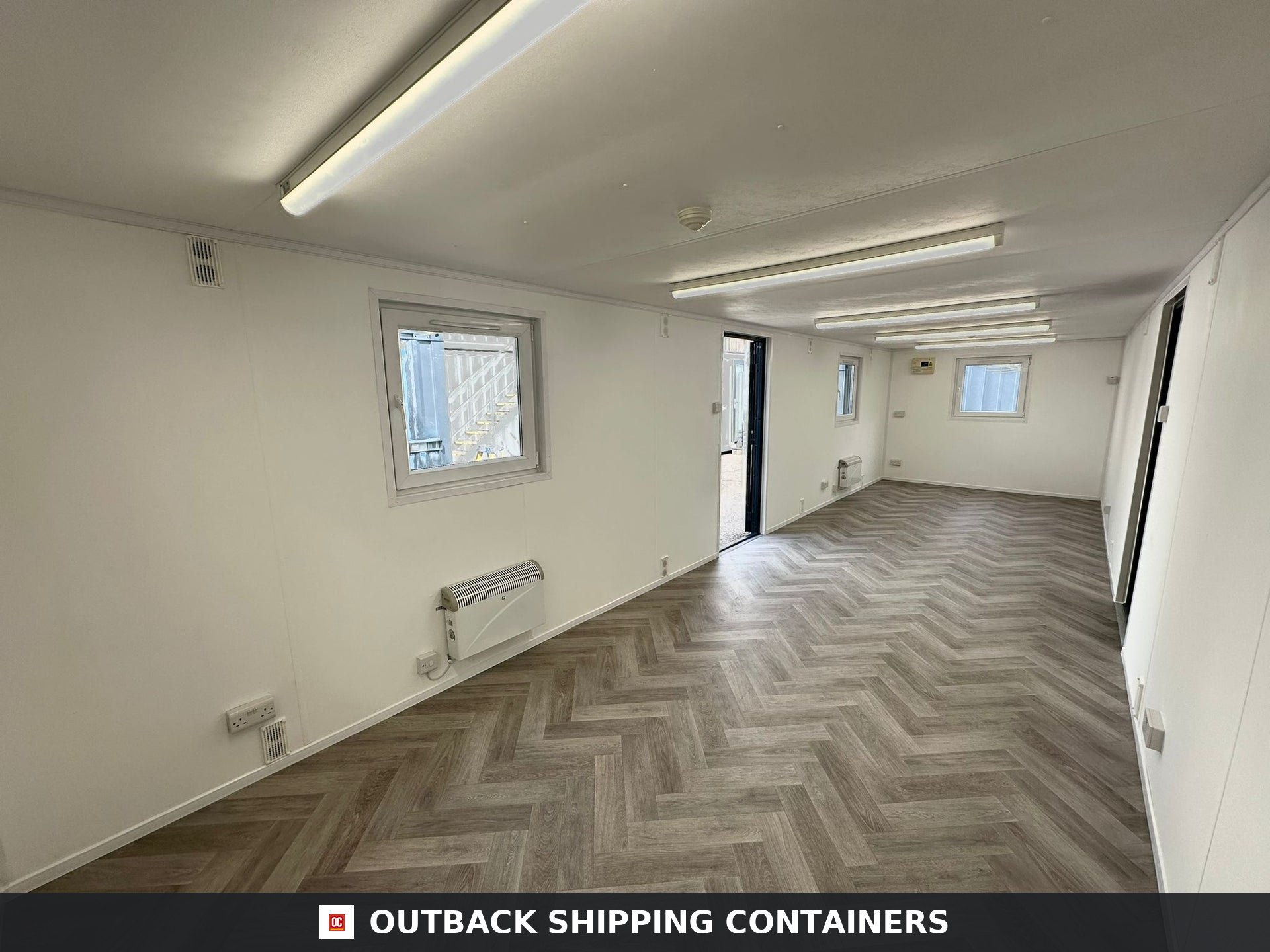 32x10ft Cabin for Sale — Interior Detail | Outback Shipping Containers 2 Interior of a refurbished 32x10ft container office with herringbone wood floors, white walls, and overhead lighting