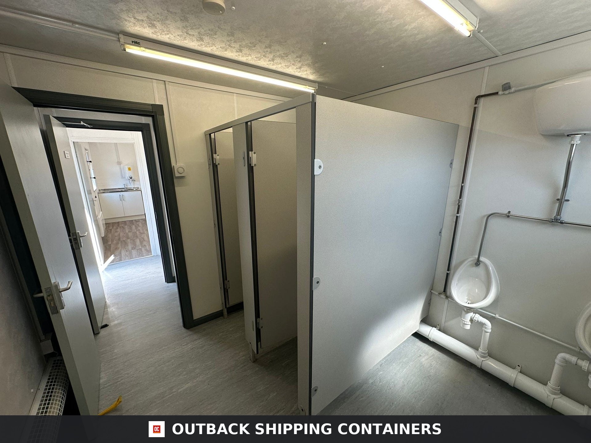 32 x 10Ft 32x10FT for Sale — Rear Exterior View | Outback Shipping Containers Interior view of a refurbished 32ft office cabin toilet block with urinals, cubicles, and overhead lighting