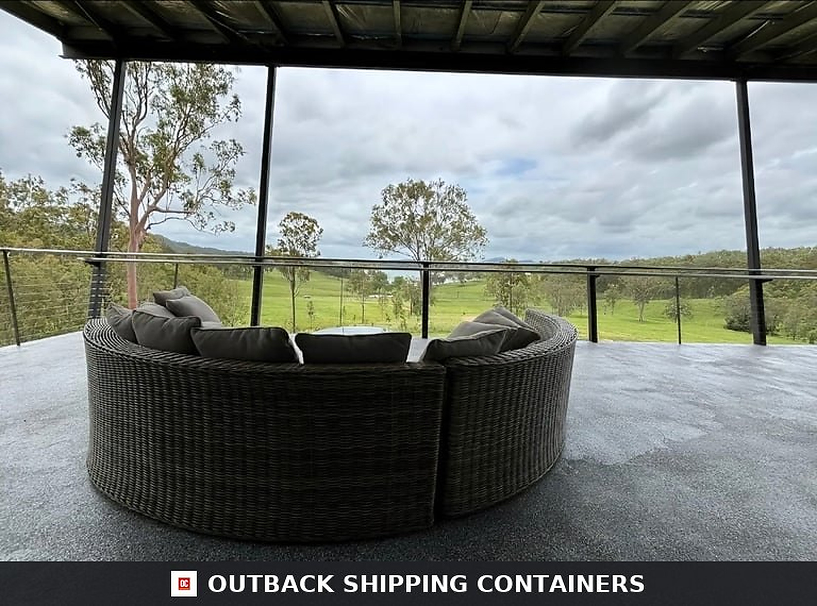 Covered upper terrace of the 3BHK container home with curved outdoor sectional sofa and glass balustrade