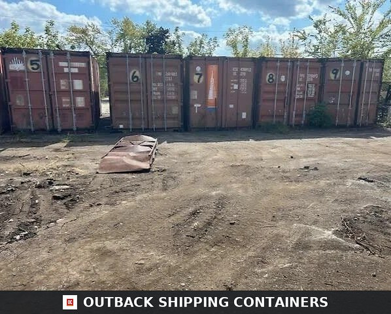 Row of numbered 20ft used shipping containers in a dirt storage lot under a blue sky