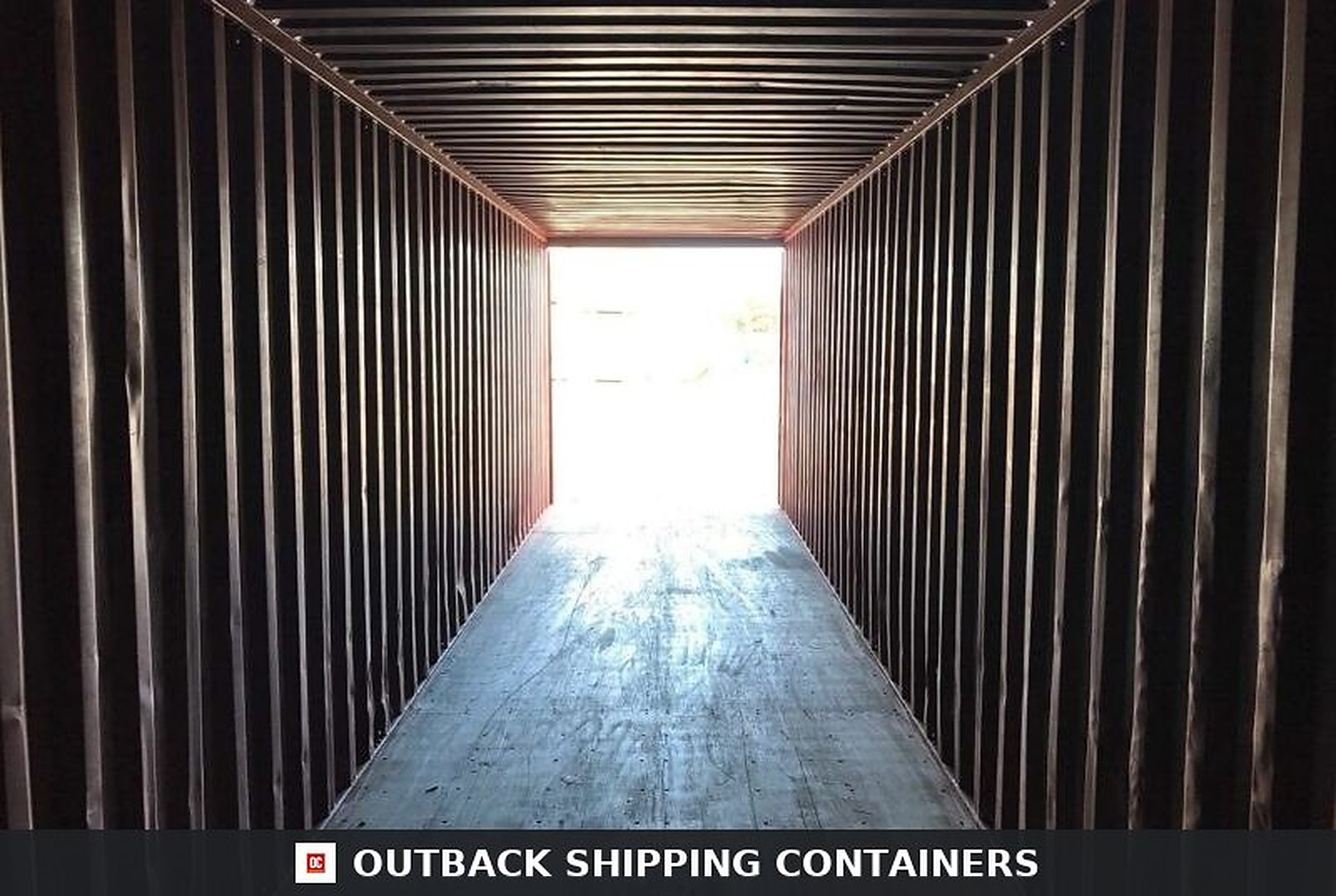Interior view of a 40ft used shipping container with corrugated steel walls and marine plywood flooring leads to a bright exit
