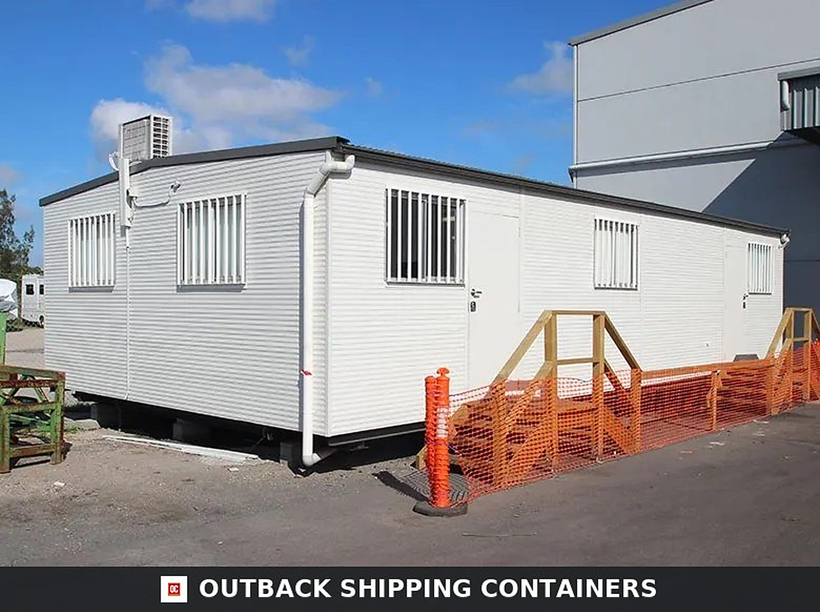 Modular portable office container with white siding, roof AC unit, and security bar windows on a gravel site