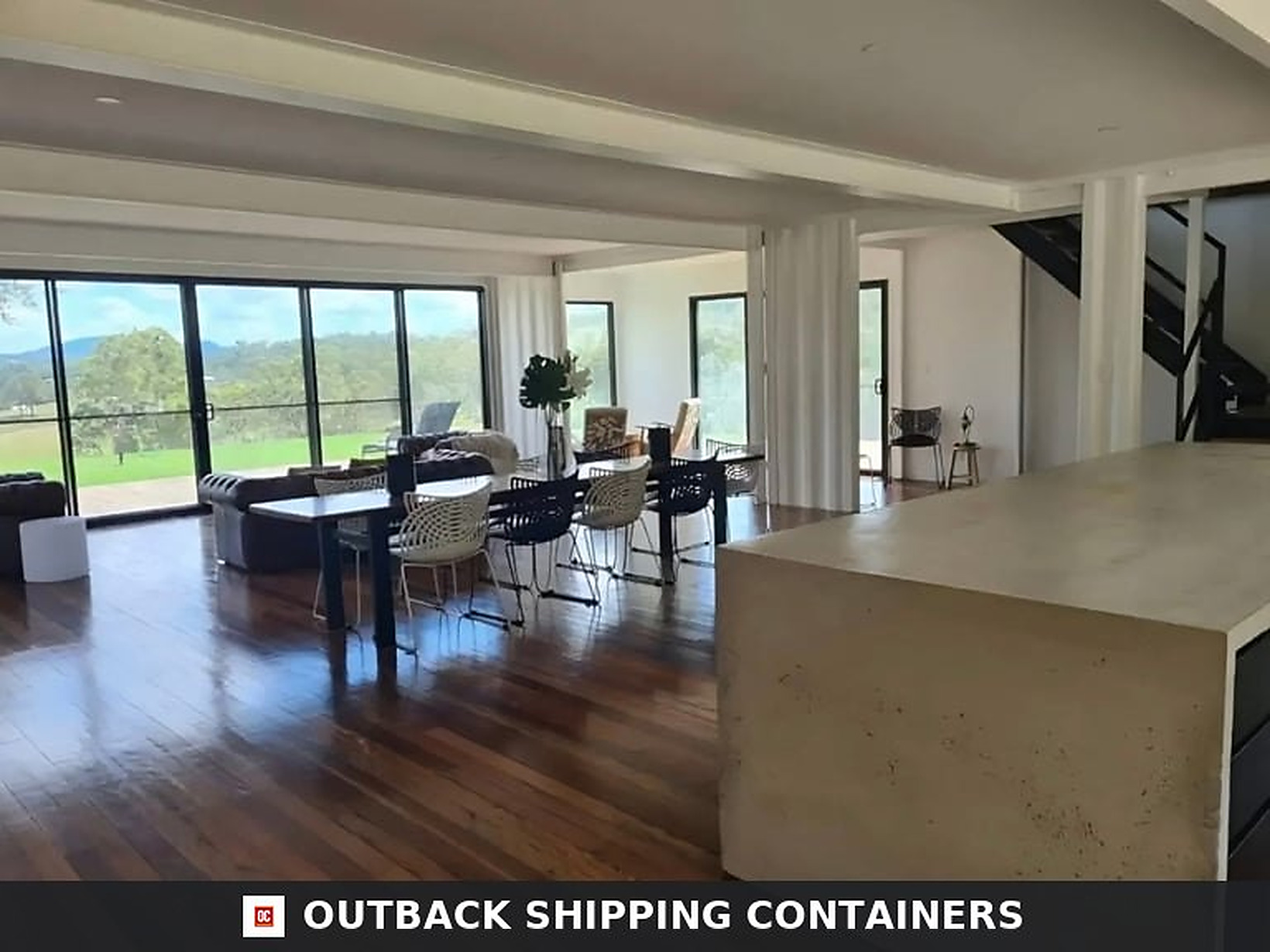 Open-plan kitchen and dining area of the 3BHK container home with concrete island bench and hardwood flooring