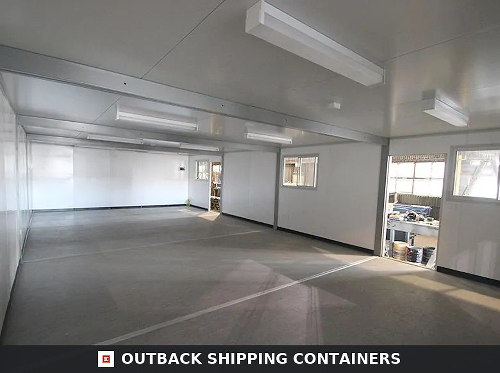Container office interior with white walls, gray commercial flooring, and fluorescent ceiling lights in a modular unit
