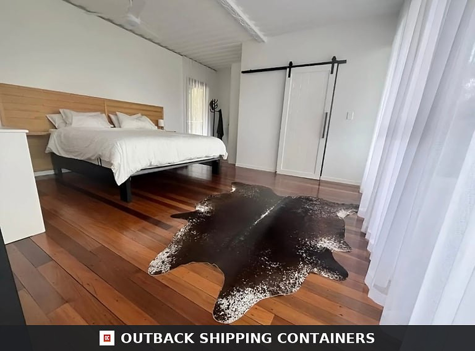Master bedroom of the two-storey container home with timber bedhead, hardwood floors and barn-style sliding door