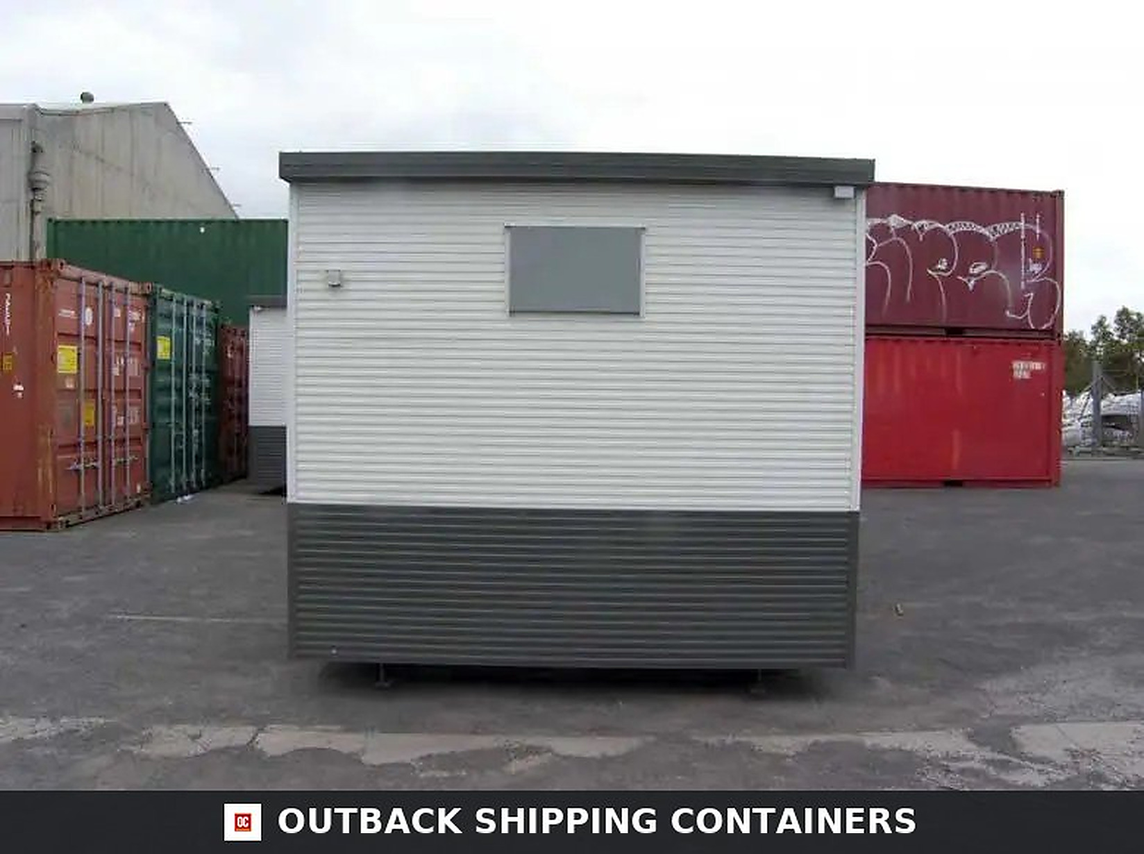 Portable Buildings – Modular Office & Storage Solutions Modular container office with white and gray corrugated siding sitting on a gravel lot near red shipping containers