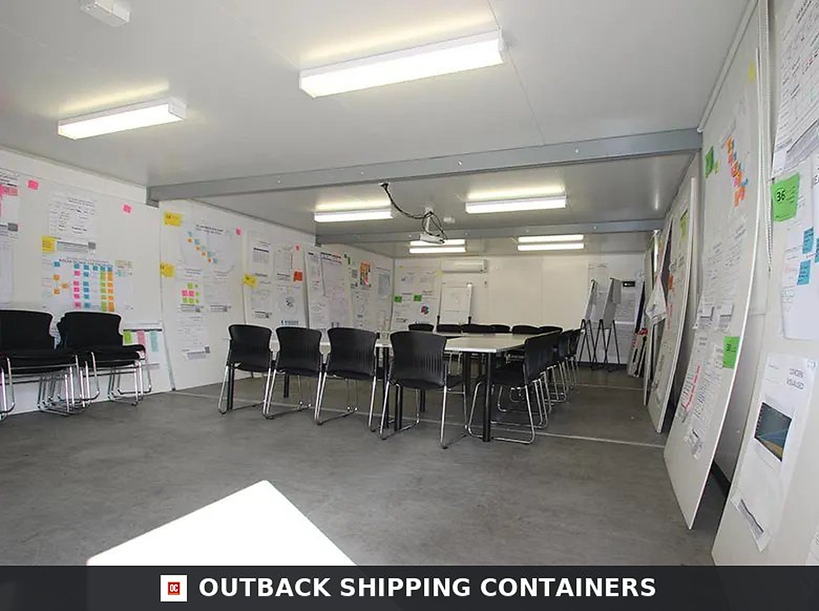 Interior of a modular container office showing a spacious white conference room with black chairs and a large table