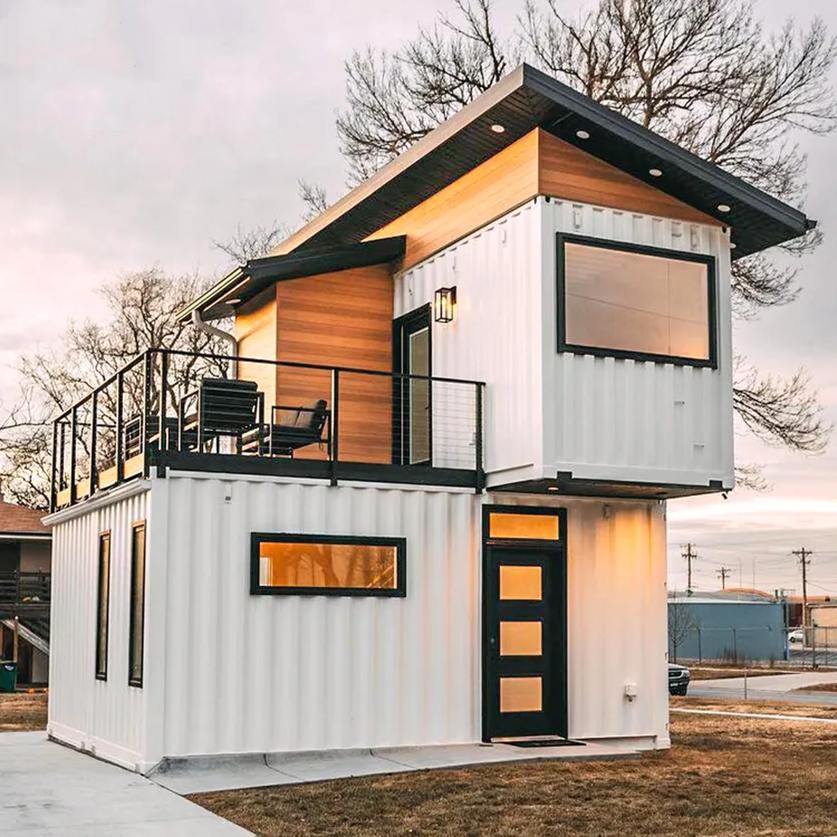 Exterior of the Duplex 3BHK container home with white corrugated steel, cedar-clad upper module and rooftop deck with black steel railing