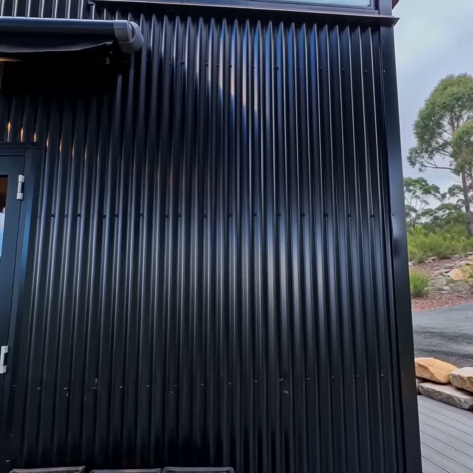 Exterior view of a black corrugated steel luxury container home featuring a modern deck and dark trim