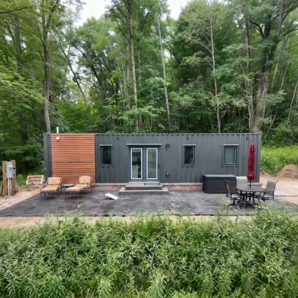 Exterior view of a charcoal gray 40ft container home with wood siding accents and a stone patio